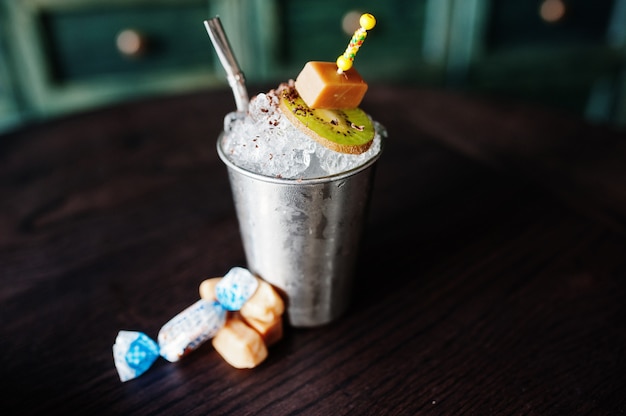 Alkoholisches Cocktail mit Bonbons und Süßigkeiten im kleinen silbernen Eimer am Bartisch
