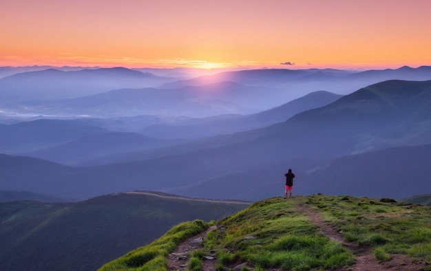 Allein Mann auf dem Berggipfel mit Blick auf das Bergtal im Nebel mit Sonnenstrahlen bei farbenfrohem Sonnenuntergang im Sommer in der Ukraine Landschaft mit reisenden nebligen Hügeln Wald erstaunlicher Himmel und Sonnenlicht Natur