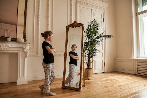 Allein süßes Teenager-Mädchen im Spiegel im Wohnzimmer zu Hause, das ihr trauriges einsames Kind sieht in seinem Spiegelbild