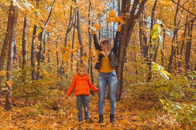 Alleinerziehende Familie, die mit Herbstlaub im Park spielt, glückliche Mutter und Sohn werfen Herbstblätter nach oben