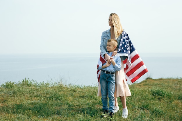 Alleinerziehende Mutter mit Sohn am Unabhängigkeitstag der USA. Frau und ihr Kind gehen mit der USA-Flagge an der Ozeanküste