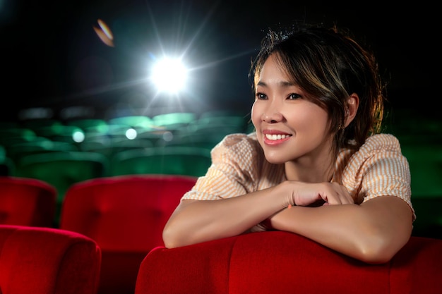 Alleinstehende asiatische Frau mittleren Alters blickt auf die Leinwand im Kino mit rotem Sitz