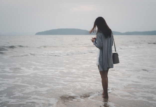 Alleinstehende Frau, die allein auf der Strandoberfläche auf einem stürmischen Meereshintergrund reflektiert