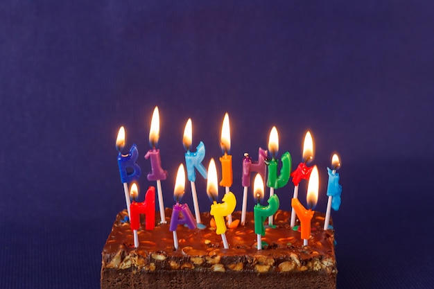 Alles Gute zum Geburtstag Brownie Cake mit Erdnüssen, gesalzenem Karamell und bunten brennenden Kerzen auf der violetten Oberfläche. Kopieren Sie Platz für Text.