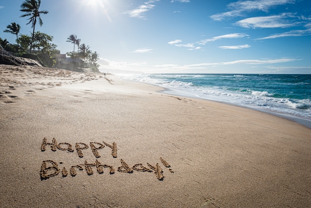 Alles Gute zum Geburtstag geschrieben im Sand am Sunset Beach in Hawaii mit Palmen und dem Ozean