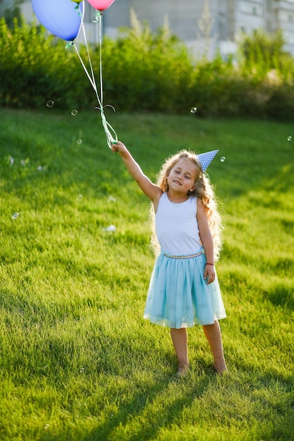 Alles Gute zum Geburtstag im Park. Ein kleines Mädchen hat Spaß mit Luftballons und in einer Mütze an ihrem Geburtstag.