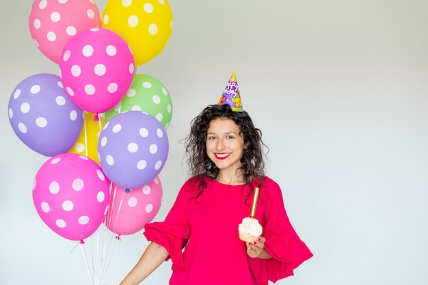 Alles Gute zum Geburtstag. Sexy brünettes Mädchen, das mit Luftballons, Feuerwerk, bunten Luftballons und Feiertagstorte auf einem weißen Hintergrund aufwirft.