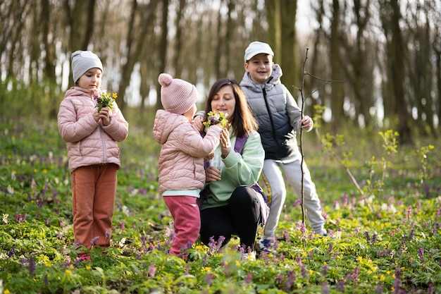 Alles Gute zum Muttertag. Wir lieben dich, Mama. Mutter mit einem Blumenstrauß und drei Kindern im frühlingsblühenden Wald