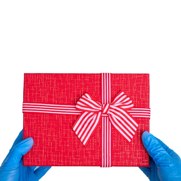 Alles Gute zum Valentinstag. Hände in blauen medizinischen Handschuhen halten eine rote Geschenkbox mit Band lokalisiert auf weißem Tisch, Quadrat, Kopienraum.