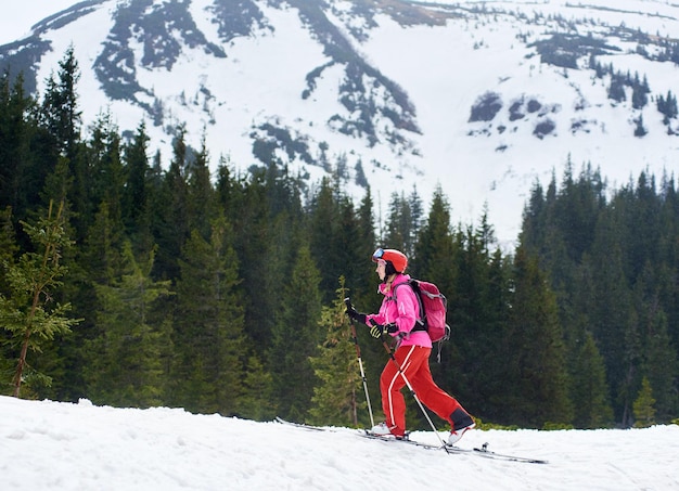 Allgemeine Seitenansicht einer jungen Backpacker-Skifahrerin im rosafarbenen Skianzug, die Winterberge erkundet und Ski fährt