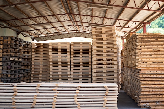 Almacén de la fábrica de aserradero con pila de paletas y tablones de madera.