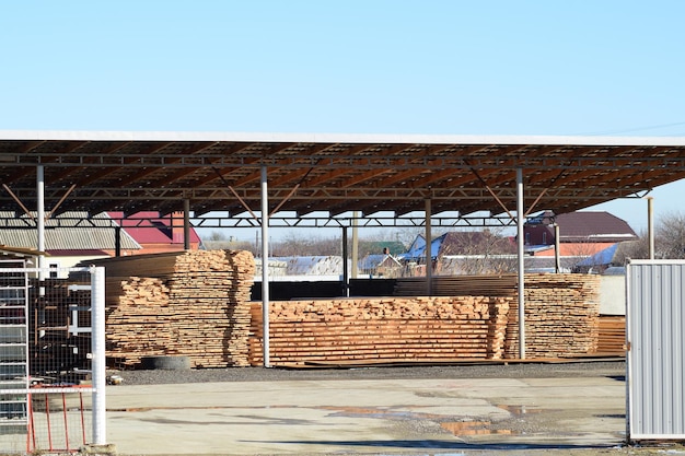 Almacén de materiales de construcción, tablones de madera apilados bajo un dosel