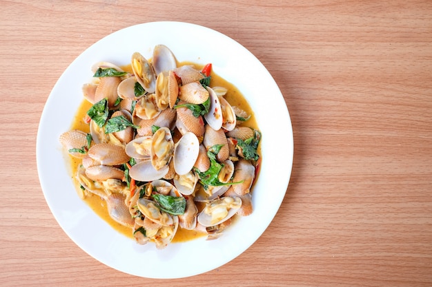 Foto las almejas salteadas en caliente con pasta de chile asado y albahaca sirven en un plato blanco sobre mesa marrón - concepto de comida casera.