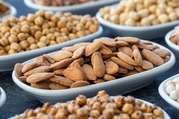 Almendra en enfoque selectivo Nueces en un plato sobre un fondo oscuro Garbanzos de nuez Garbanzos blancos Pistacho de anacardo de almendra de morera seca Tipos de nueces en el plato