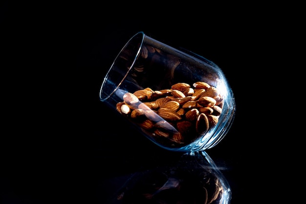 Almendra pelada en un cubo de copa de vino de tarro sobre un fondo negro aislado Fila de tazones con vista frontal de almendras y nueces