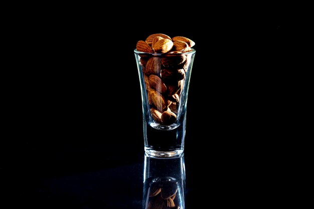 Almendra pelada en un cubo de copa de vino de tarro sobre un fondo negro aislado Fila de tazones con vista frontal de almendras y nueces