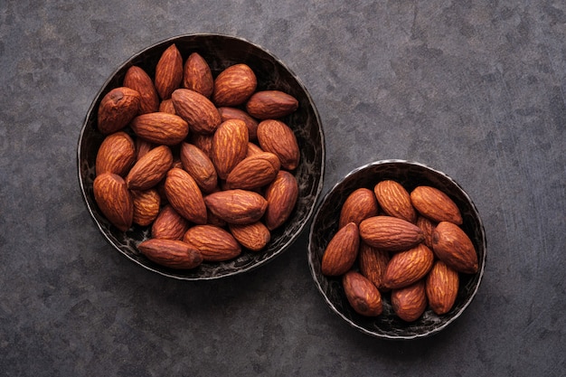 Almendras en dos cuencos sobre fondos oscuros.