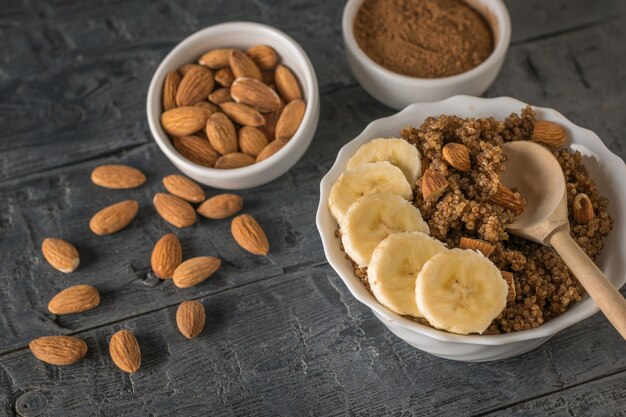 Almendras esparcidas, gachas de quinua con plátano sobre una mesa rústica. Dieta saludable. Endecha plana.