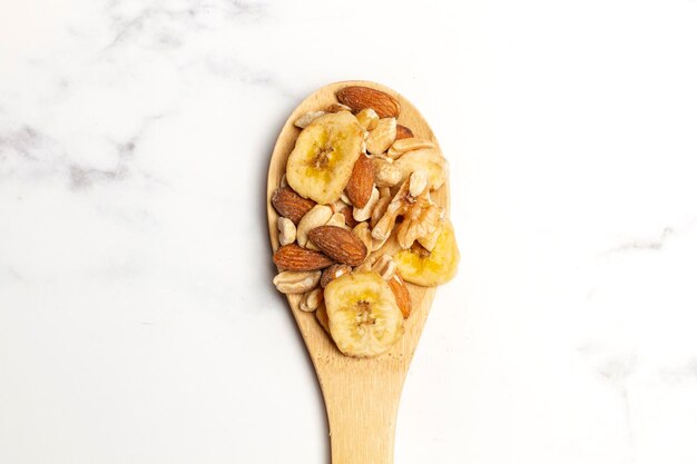 Almendras, nueces, cacahuetes y rodajas de plátano seco en una cuchara de madera y en un mostrador de cocina blanco