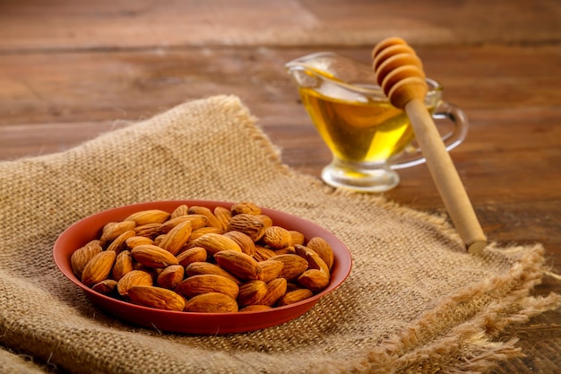 Almendras en un plato de saqueo junto a la miel con una cuchara sobre una mesa de madera.