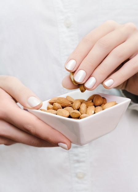 Foto almendras en un tazón blanco en manos de mujer