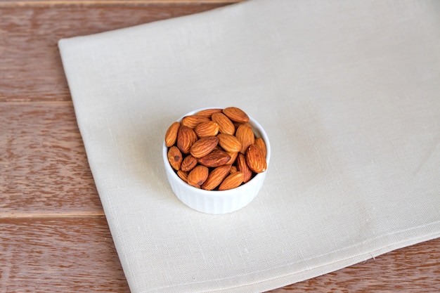 Almendras tostadas en tazón de porcelana blanca sobre servilleta textil y mesa de madera marrón