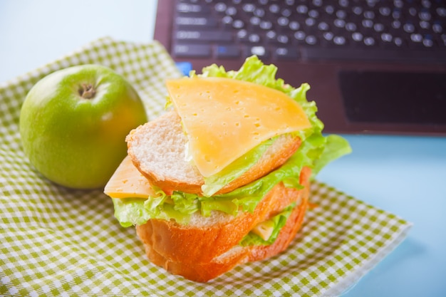 Almoce com sanduíche e maçã verde e portátil na tabela.