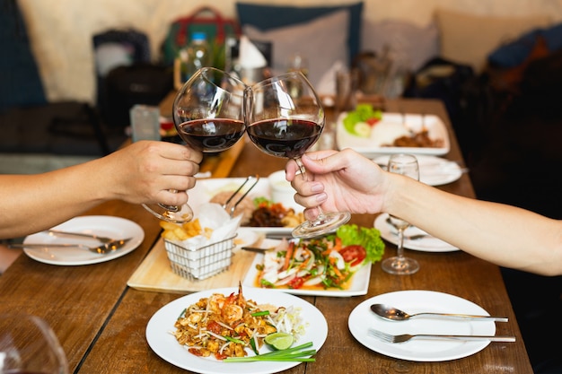 Almoço da celebração dos amigos com as mãos que brindam o vinho tinto de vidro com alimento.