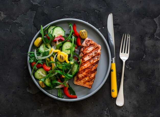 Foto almoço de dieta delicioso jantar de salmão grelhado e salada de vegetais frescos em um fundo escuro vista superior