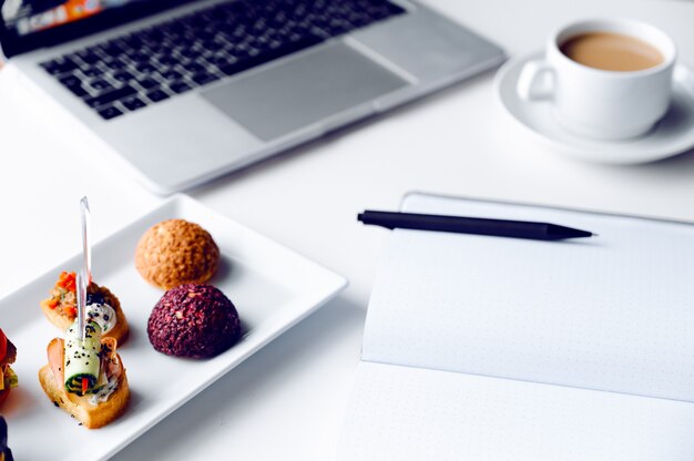 Almoço de negócios no escritório, coockies de lanches de comida na mesa de madeira branca perto do computador portátil.