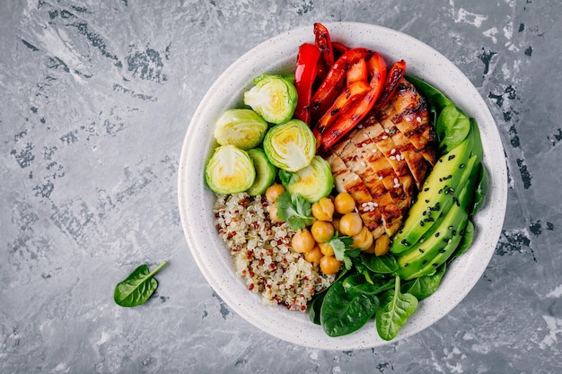 Almoço de tigela de buda vegetal saudável com frango grelhado e quinoa espinafre abacate couve de Bruxelas páprica vermelha e grão de bico em fundo cinza Vista superior