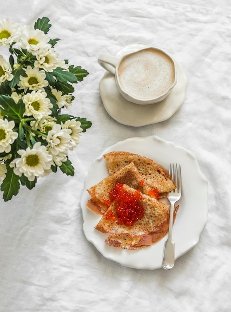 Foto almoço delicioso servido crepes com caviar vermelho cappuccino buquê de crisântemos em um fundo claro vista de cima