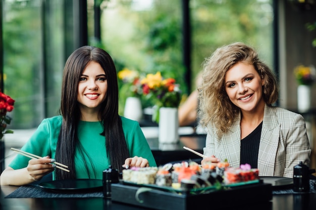 Foto almoço em restaurante chinês na esplanada. meninas loiras e morenas comem sushi com palitos chineses. conceito de tempo de sushi.