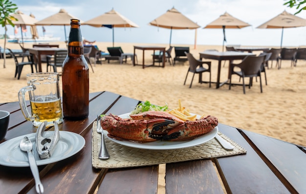 Almoço em um restaurante de praia com casca de caranguejo cozido, batata frita, salada em um prato branco e cerveja gelada