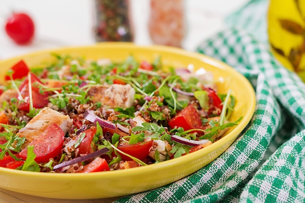 Almoço na tigela de salada com frango e quinoa grelhados, tomate, pimentão, cebola roxa e rúcula em branco.