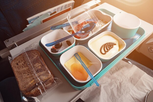 Almoço no avião: pão, carne com legumes e arroz, pedaços de queijo, damasco seco, salada e bebida na xícara, closeup.