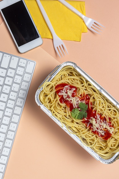 Foto almoço no local de trabalho espaguete caseiro e saudável com tomate e queijo na mesa de trabalho com teclado de computador. comida em casa para o conceito de escritório. comida para levar