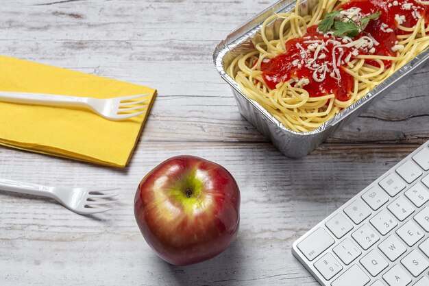 Almoço no local de trabalho espaguete caseiro e saudável com tomate e queijo na mesa de trabalho com teclado de computador. Comida em casa para o conceito de escritório. Comida para levar