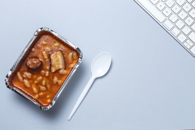 Almoço no local de trabalho Feijão com chouriço e carne em recipiente de alumínio na mesa. Entrega de alimentos