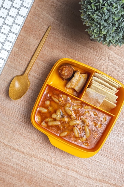 Almoço no local de trabalho Feijão com chouriço e carne na lancheira na mesa. Entrega de alimentos