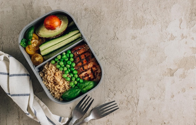 Foto almoço saudável em recipientes de plástico com quinoa, tomate, frango, abacate, pepino, ervilhas verdes, folhas de manjericão sobre fundo de concreto vista superior com espaço de cópia