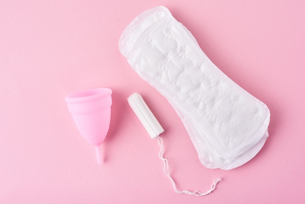 Foto almofada sanitária, copo menstrual e tampão em um fundo rosa