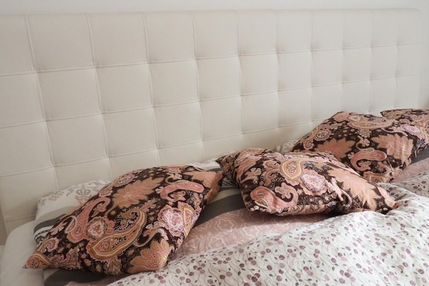 Almofadas decorativas rosa na roupa de cama Cama de casal com travesseiros e edredom de penas grossas Design de quarto Cabeceira branca macia Interior com móveis e roupas de cama