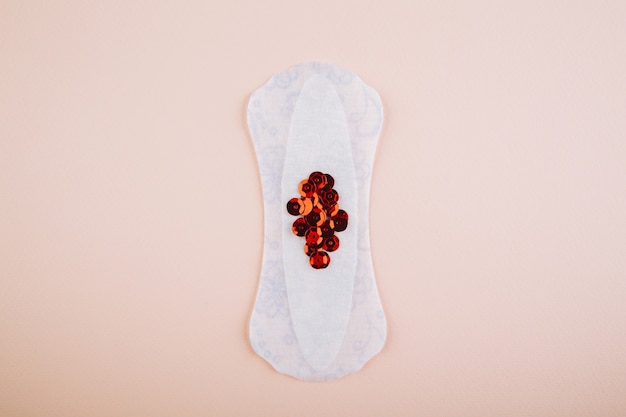 Almofadas menstruais com glitter vermelho brilhante em fundo rosa. Ciclo de períodos da mulher, frequência da menstruação. Conceito de fotografia de natureza morta minimalista.