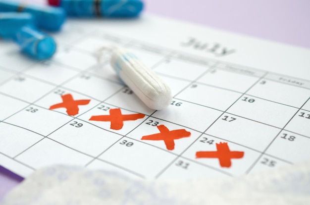 Almofadas menstruais e tampões no calendário do período menstrual com marcas da cruz vermelha encontram-se no fundo lilás