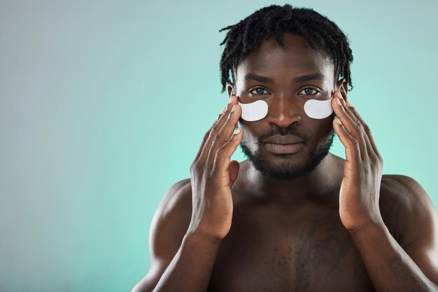 Almofadas oculares para cuidados com a pele e retrato de um homem negro em estúdio para uma rotina facial saudável e cosmética natural Bem-estar da saúde e cara africano com um tratamento facial de fundo azul com espaço de maquete