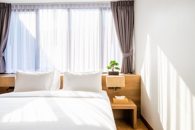 Almohada blanca en la decoración de la cama con lámpara de luz y árbol verde en macetas en el interior de la habitación del hotel