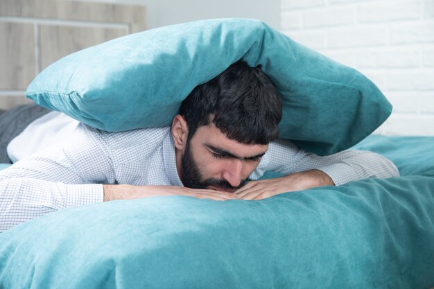 Almohada de hombre triste en la cabeza en la cama