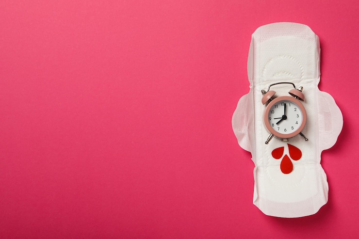 Almohadilla menstrual con reloj y gotas rojas sobre fondo rosa