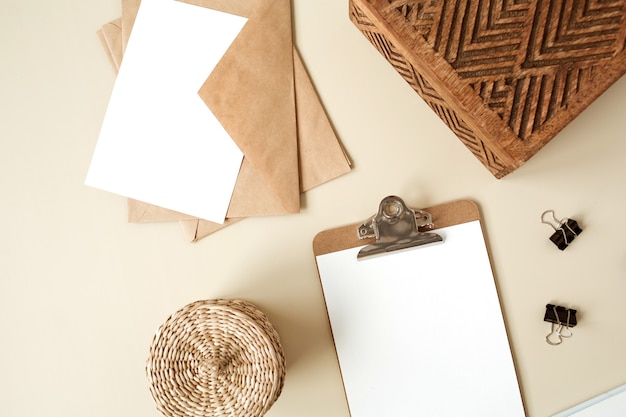 Almohadilla de tableta portapapeles con hoja de papel en blanco sobre mesa beige. Endecha plana, vista superior